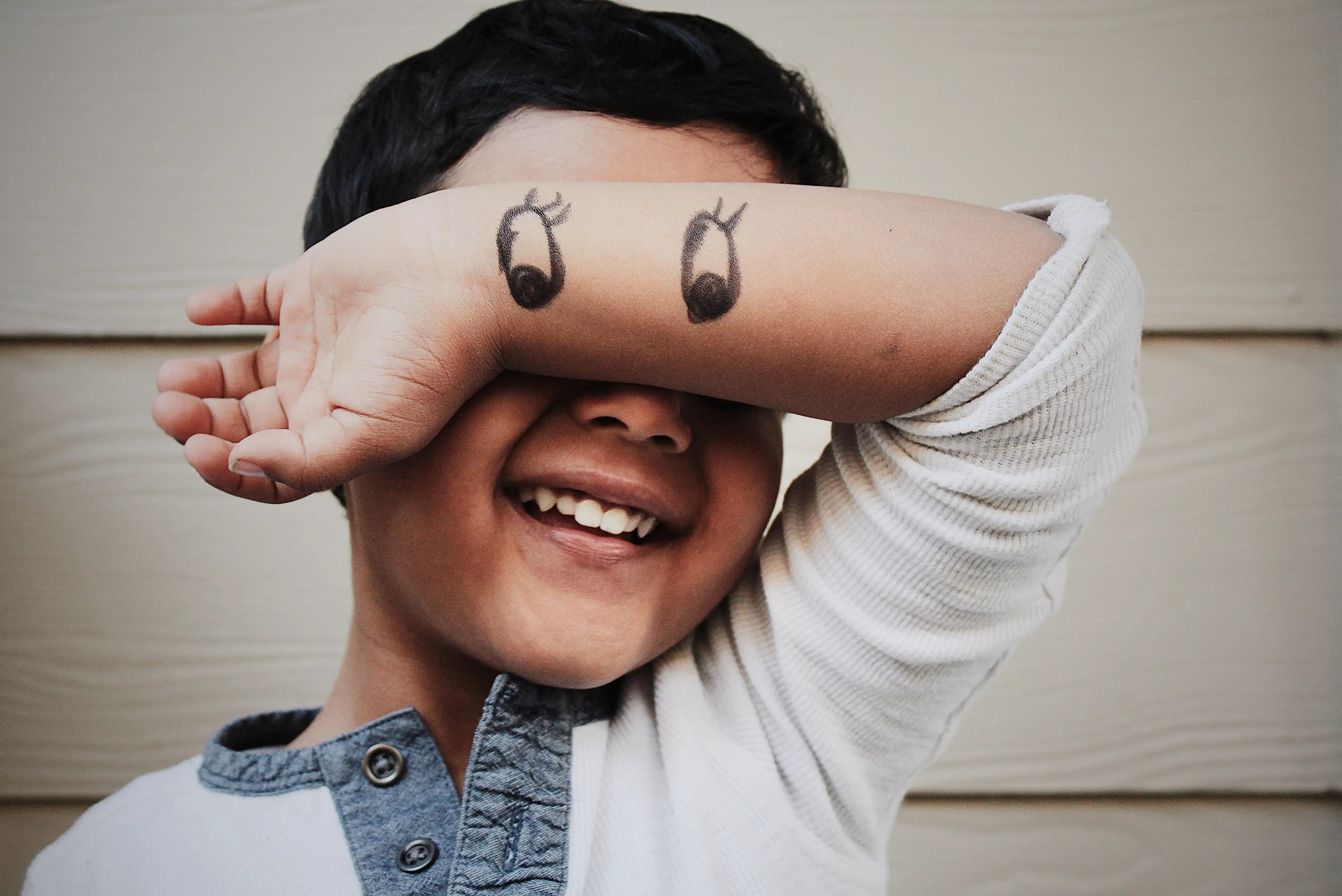 child hiding behind their own hands